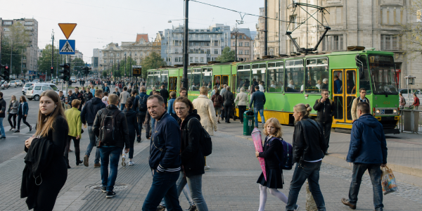 Wrześniowy poranek w mieście – ludzie spieszą się w różnych kierunkach przy przystanku tramwajowym i ruchliwym skrzyżowaniu, a część przechodniów patrzy w obiektyw.