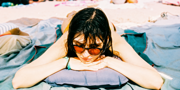 Kobieta z mokrymi włosami odpoczywająca na plaży w pełnym słońcu – ochrona włosów latem podczas częstych kąpieli